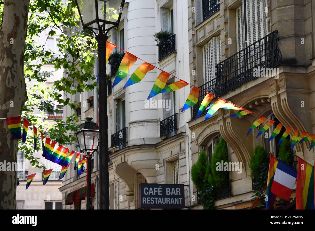 Decoration of triangle shape banners in colors of Lgbtq flags hanging between vintage lantern streetlights and ornate stone house with balconies. Gay Stock Photo