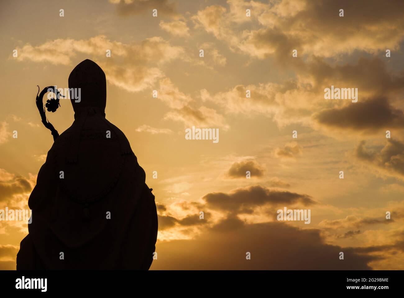 Christian Religion and Spirituality. Bishop ancient statue silhouette with crosier against a sunset sky Stock Photo