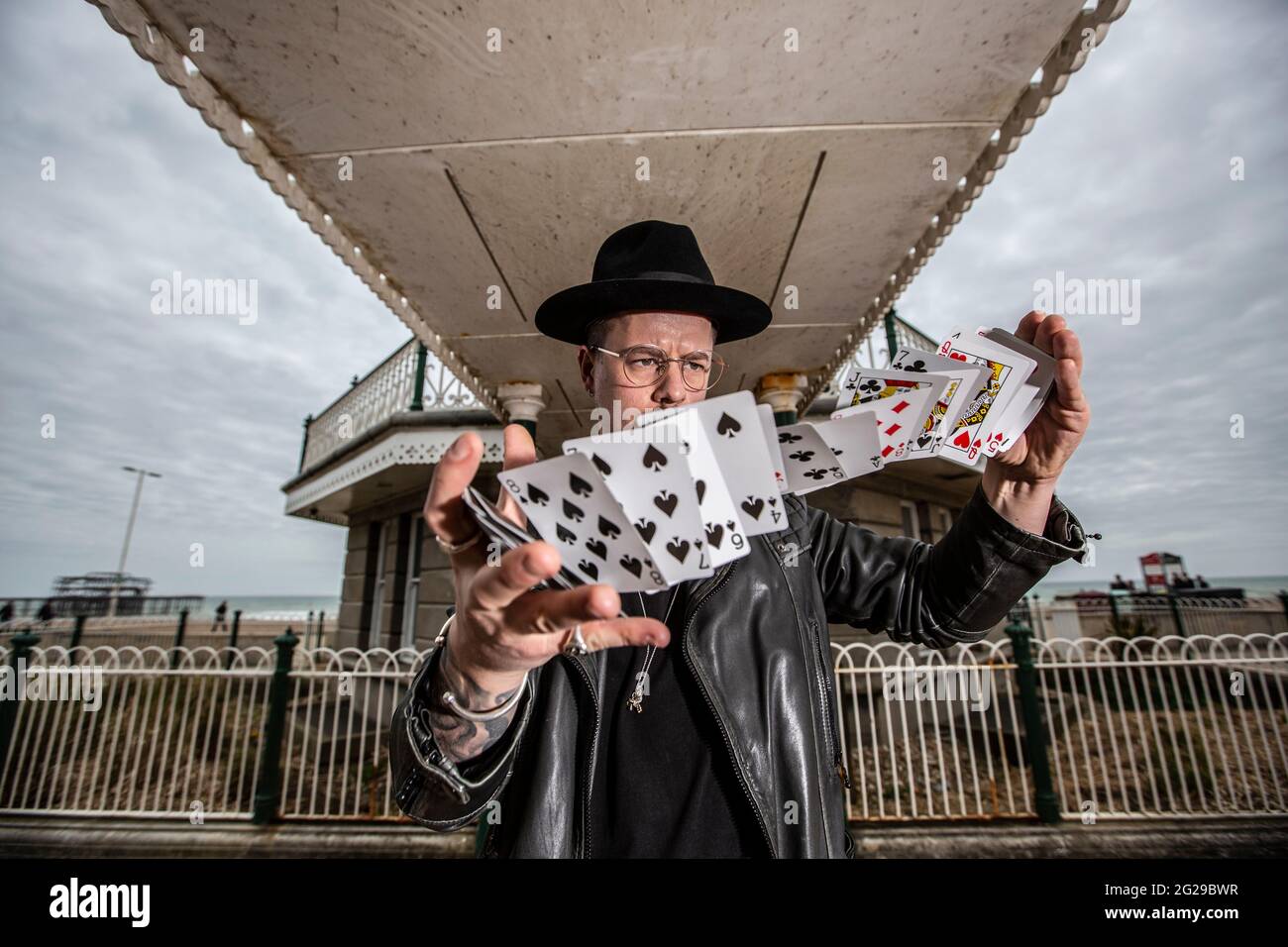 Magician Guy Parker attempts a Card Spring Flourish on a windy day along the Brighton seafront, Sussex, England, United Kingdom Stock Photo