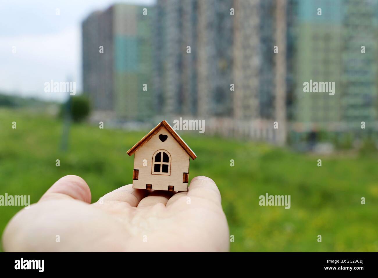 Real estate agent, wooden house in male hand on background of residential buildings. Purchase or rental home, housing in ecologically clean suburb Stock Photo
