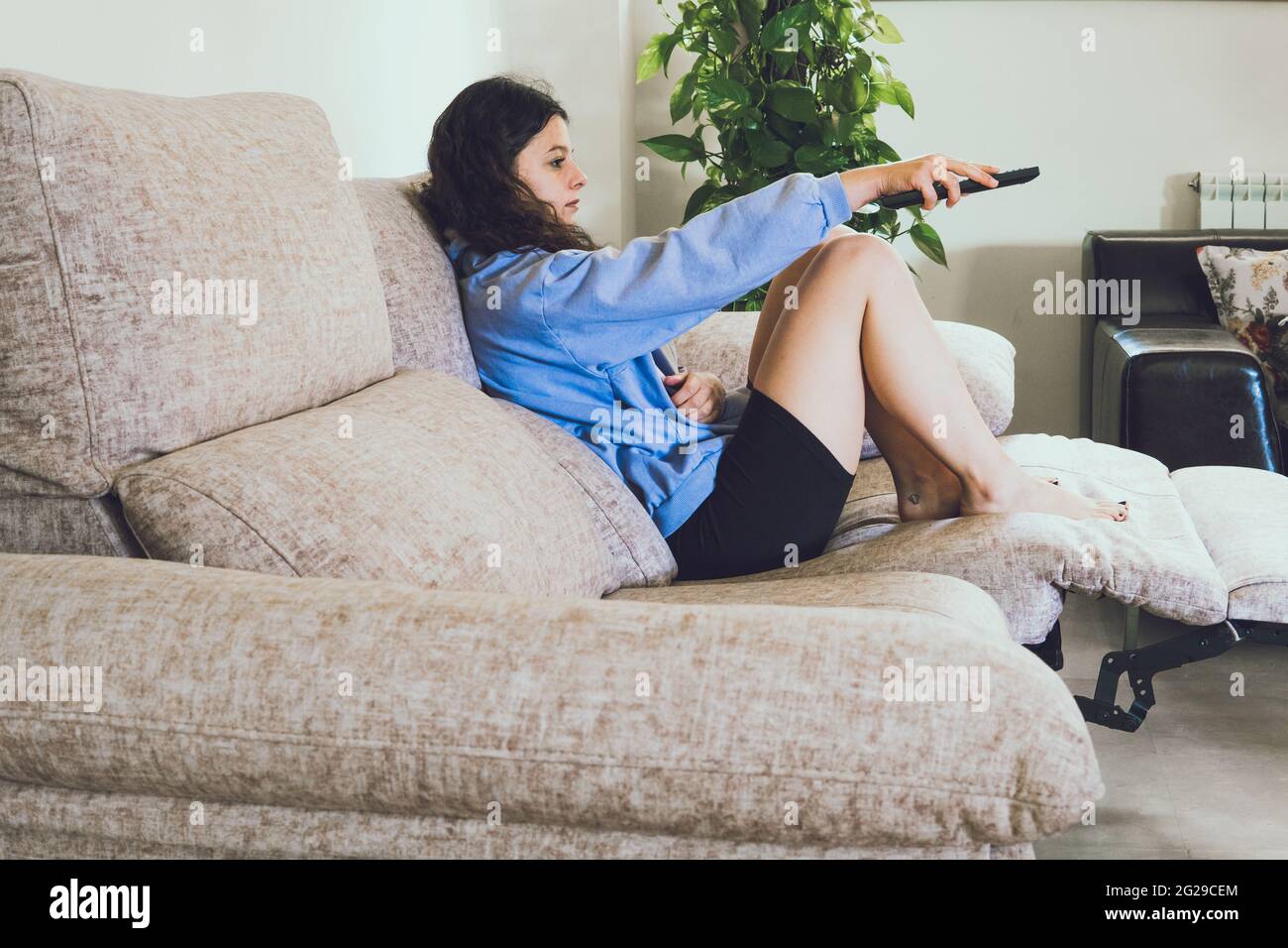 woman on the sofa changing the channel with the remote Stock Photo