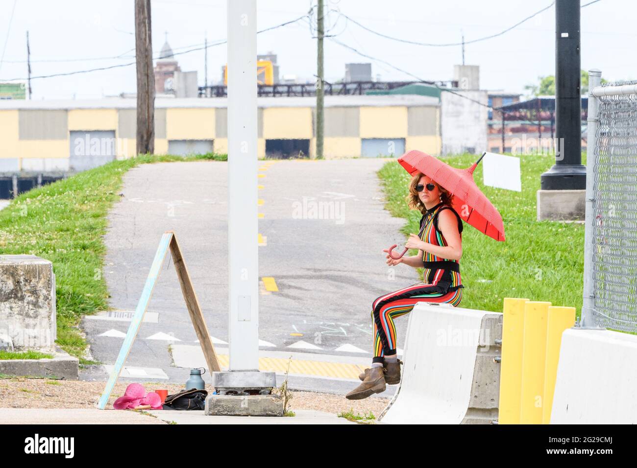 NEW ORLEANS, LA, USA - MAY 9, 2021: Woman in colorful pant suit sits on concrete barricade holding an umbrella Stock Photo