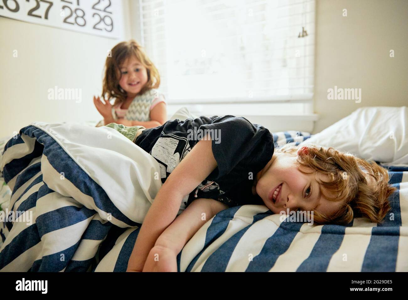Portrait of smiling boy lying by sister on bed in bedroom at home Stock Photo