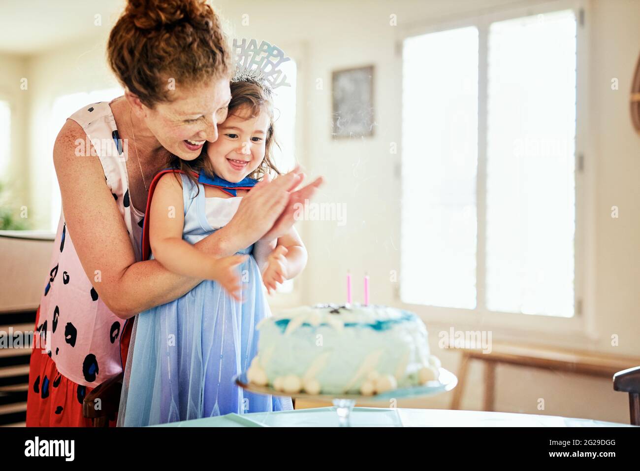 Happy mother clapping while celebrating birthday of daughter at home Stock Photo