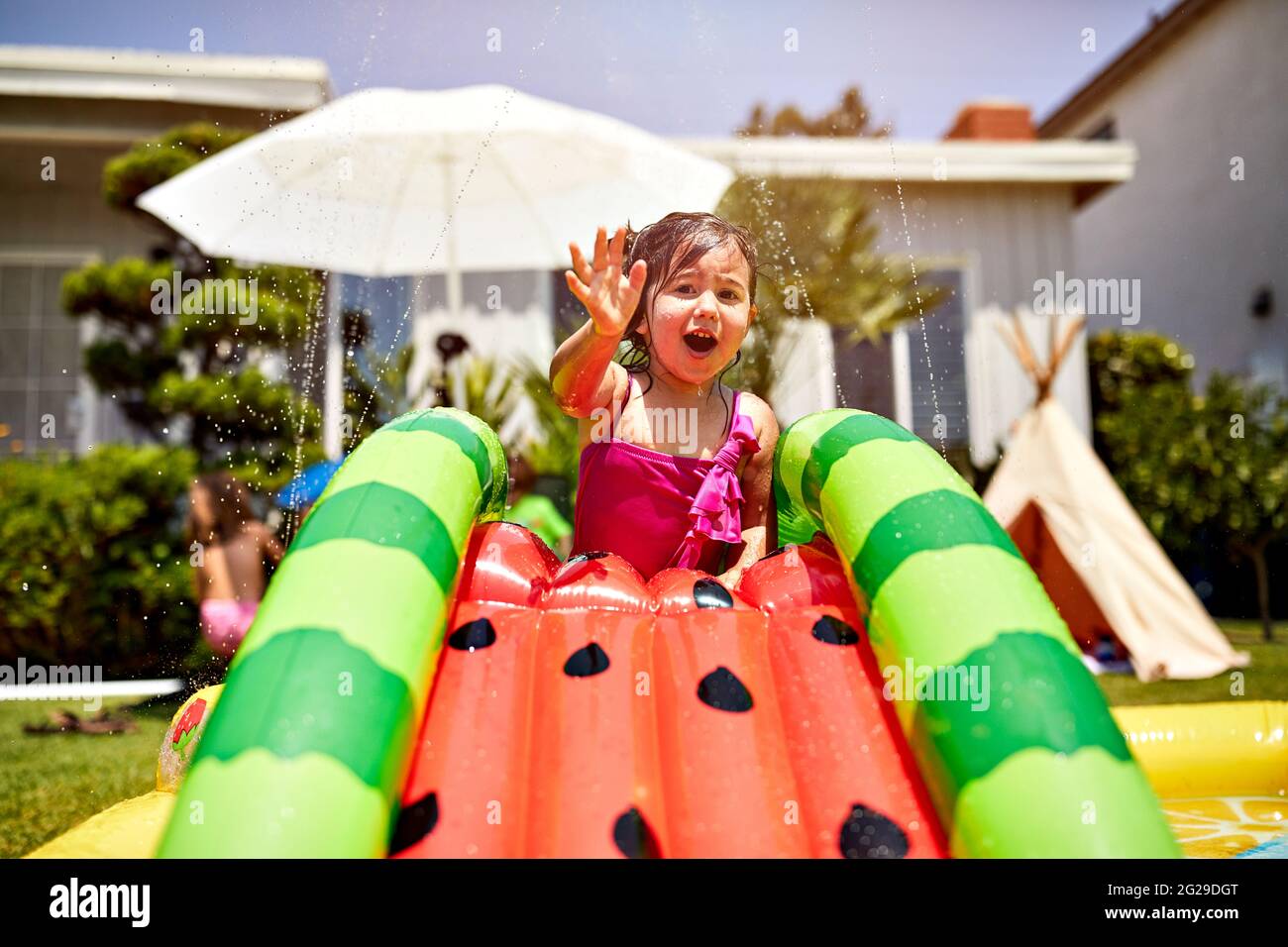 Girl playing on wet inflatable slide in backyard Stock Photo