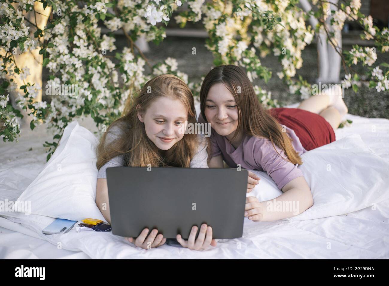 Teen girls looking at laptop lying on bed in the garden Stock Photo