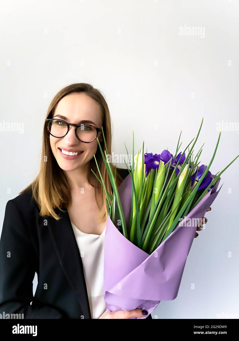 Portrait of a businesswoman with an open smile in glasses with a bouquet of flowers against the white wall Stock Photo