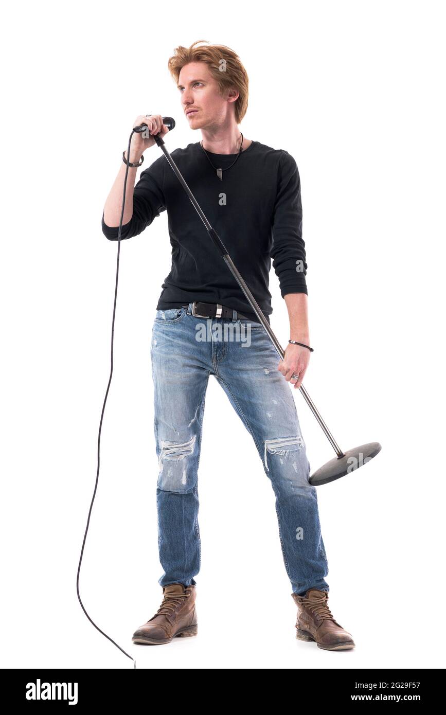 Handsome singer in jeans holding microphone posing and looking away. Full body length isolated on white background. Stock Photo
