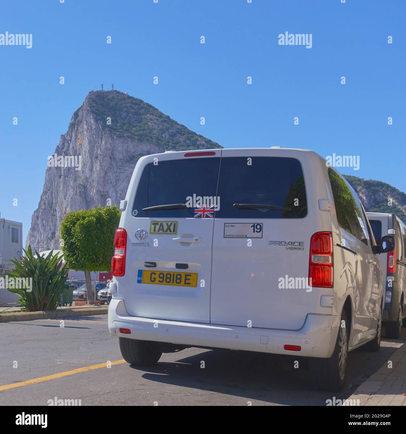 A Gibraltar taxi, with a Union Jack sticker, close to the border with Spain sits under a cloudless blue sky backed by the Rock Stock Photo