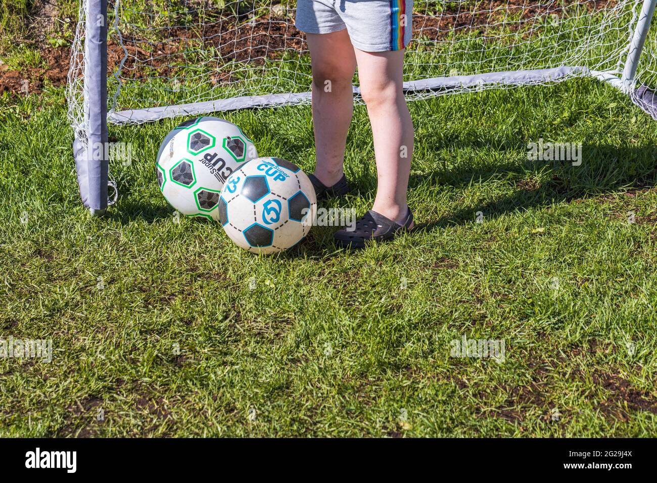 Close up view of the child's feet near two balls on football goal background. Stock Photo