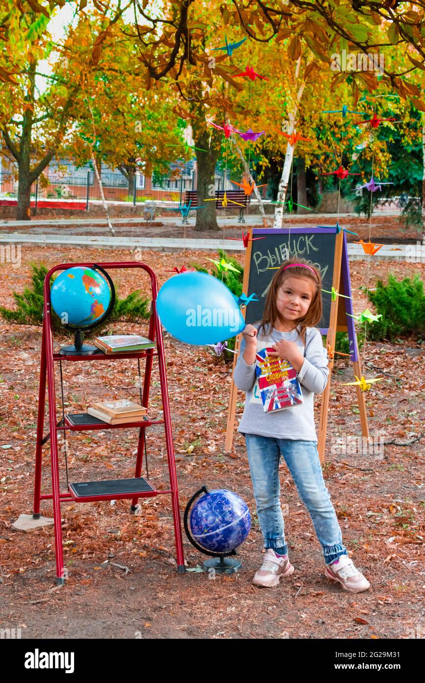 Lisichansk. Ukraine 04.10.2020 Little schoolgirl with a blue balloon against the background of an autumn park against the background of a school board Stock Photo
