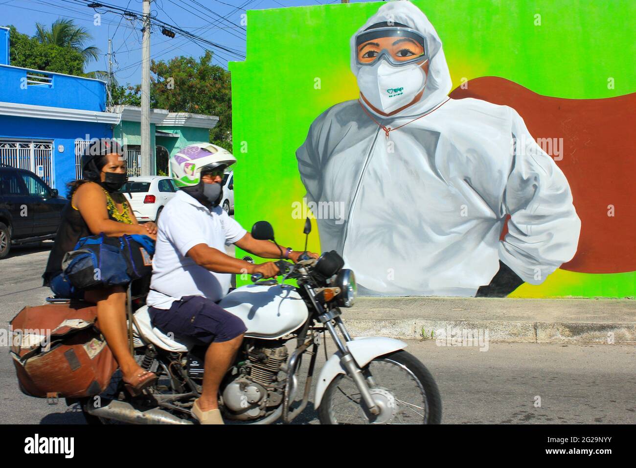 People on a motorcycle pass in front of mural celebrating healthcare workers as Covid-19 Heroes, Merida Mexico Stock Photo
