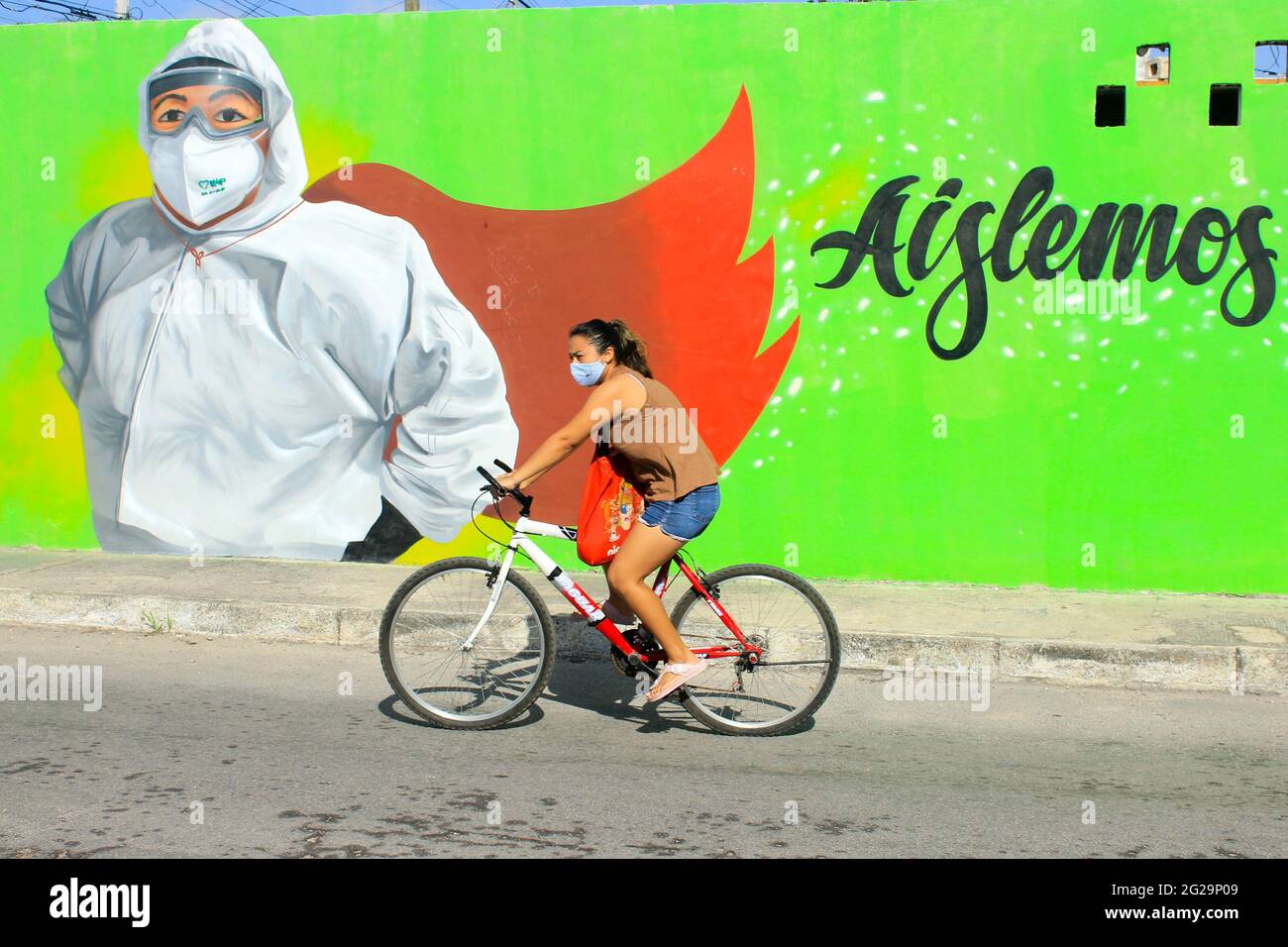 Mexican cyclist wearing a face mask passes in front of mural celebrating healthcare workers as Covid-19 Heroes, Merida Mexico Stock Photo