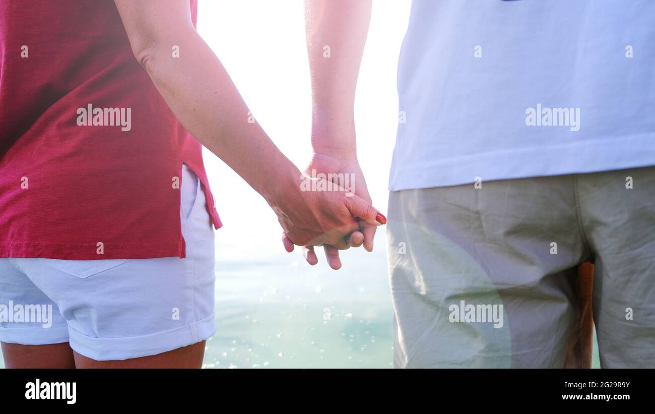 Couple holding hands at sunset on beach. Romantic young couple in love Stock Photo