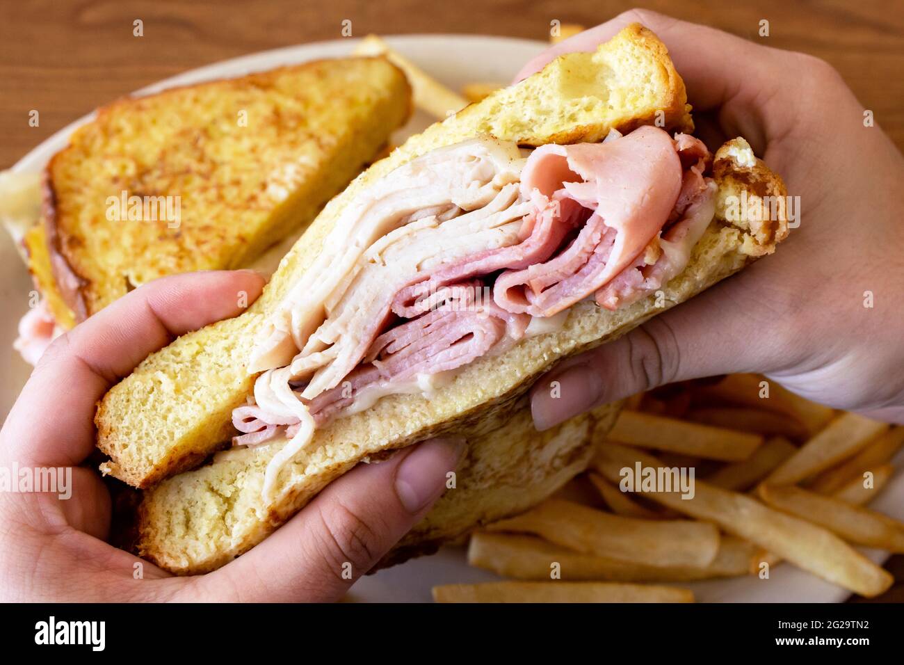 A monte cristo sandwich is being held over a white plate with the other half of the sandwich in view and french fries. Stock Photo