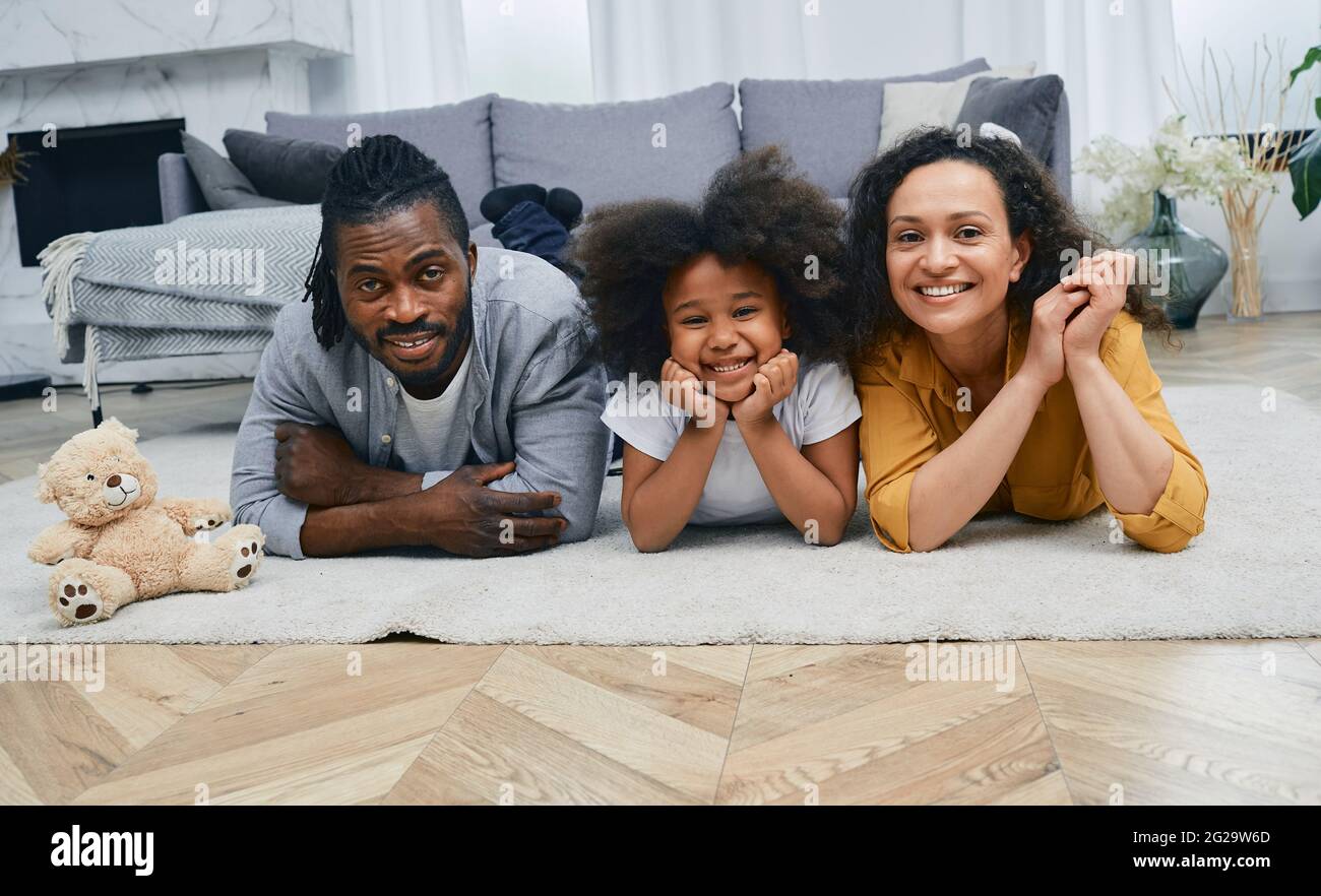 Buying or renting a house for a young family with a child. Happy mixed race family lying on floor of their new home after moving Stock Photo