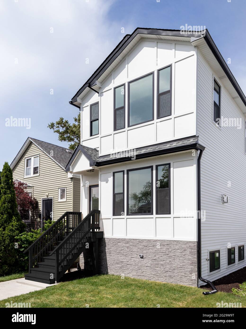 A new, white modern farmhouse with a dark shingled roof and black window frames. The bottom of