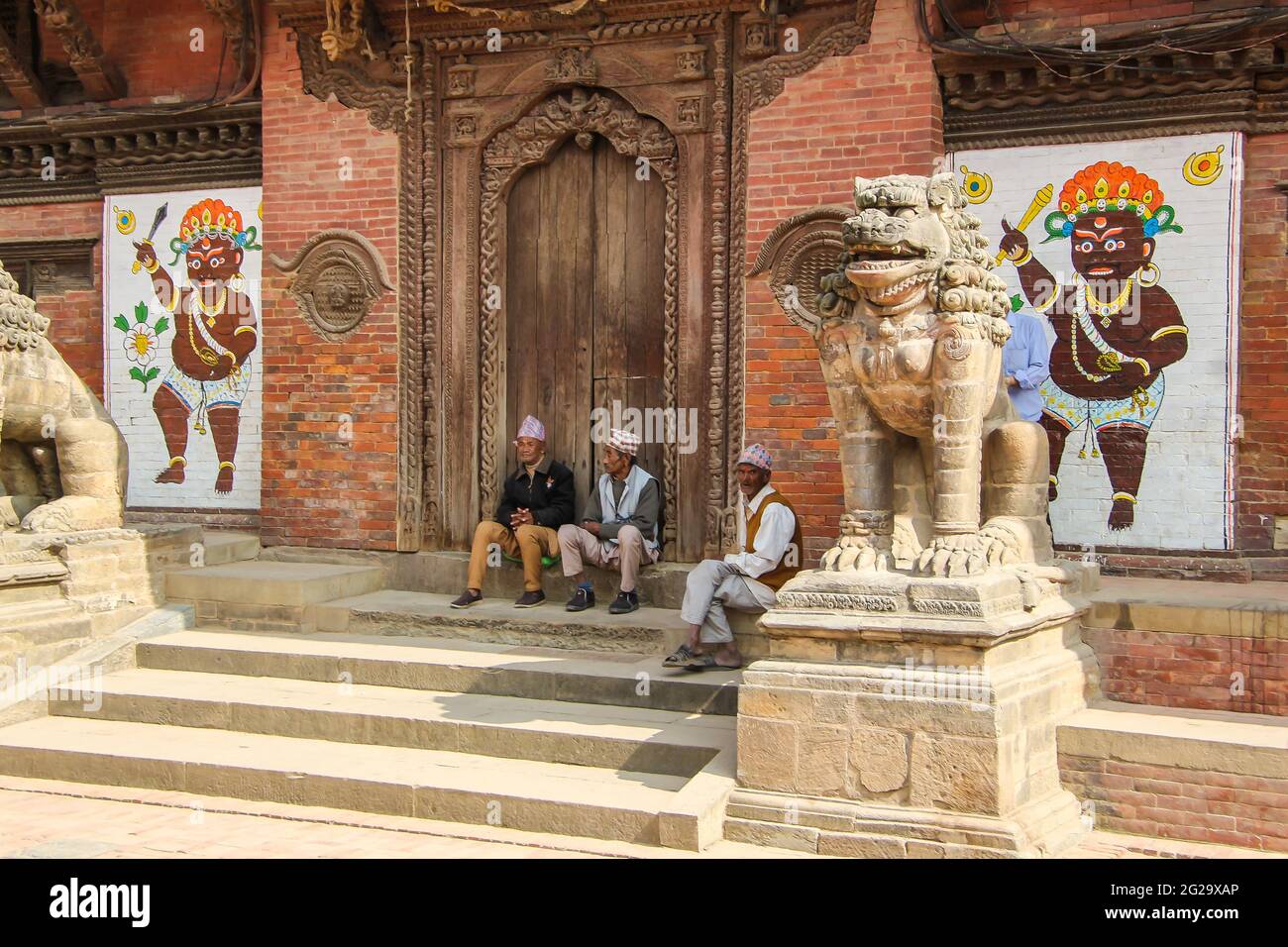 A group of Nepali men relax outside a historic building in Patan, Kathmandu, Nepal. They are wearing the dhaka topi - the traditional Nepali hat. Stock Photo