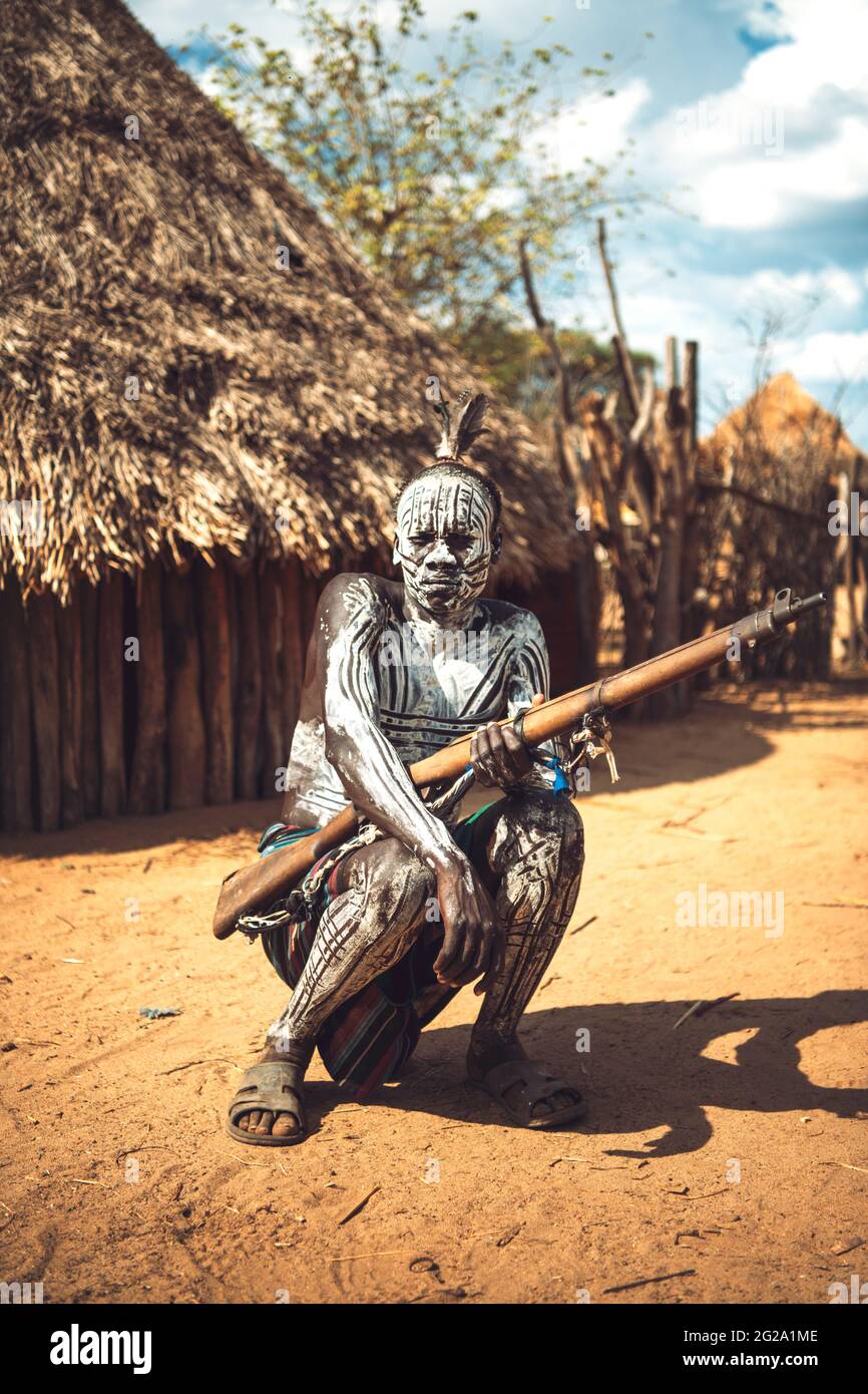 man with painted body holding a shotgun in Karo tribe village. Omo Valley, Ethiopia Stock Photo