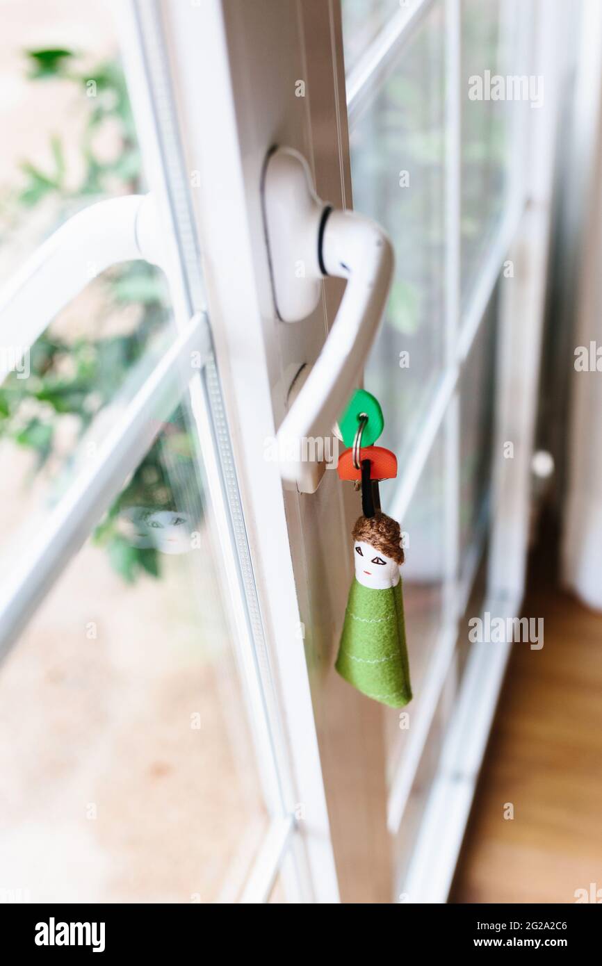 Funny triangular shaped human keychain with keys sticking out from lock of transparent balcony door of modern apartment Stock Photo