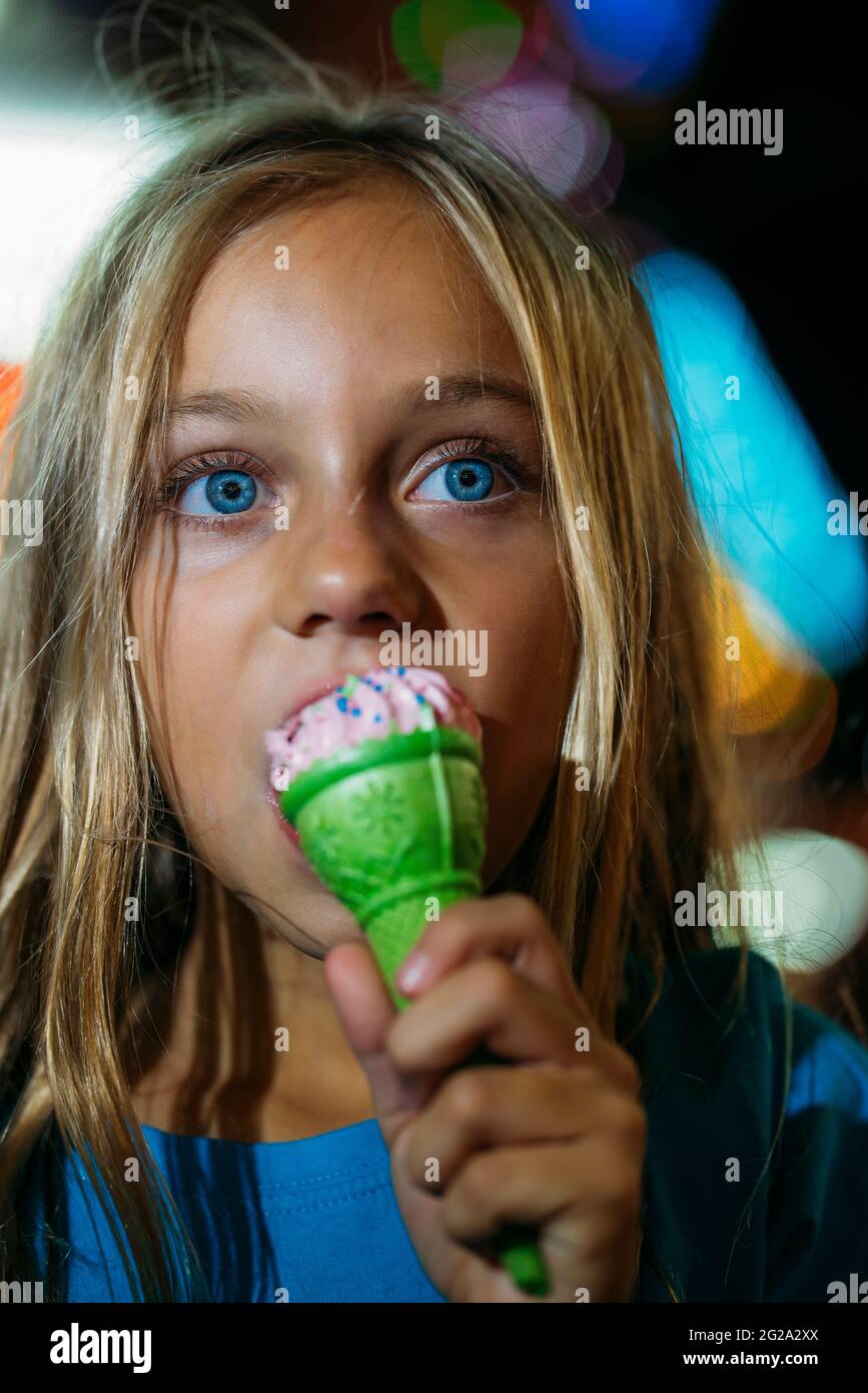 Little blonde girl eating a delicious ice cream in amusement park by