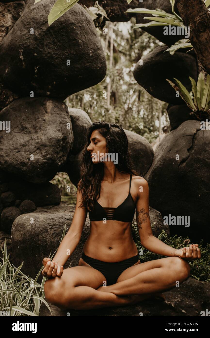 Attractive concentrated ethnic female in black bikini doing yoga pose  sitting and meditating alone among cliffs Stock Photo - Alamy
