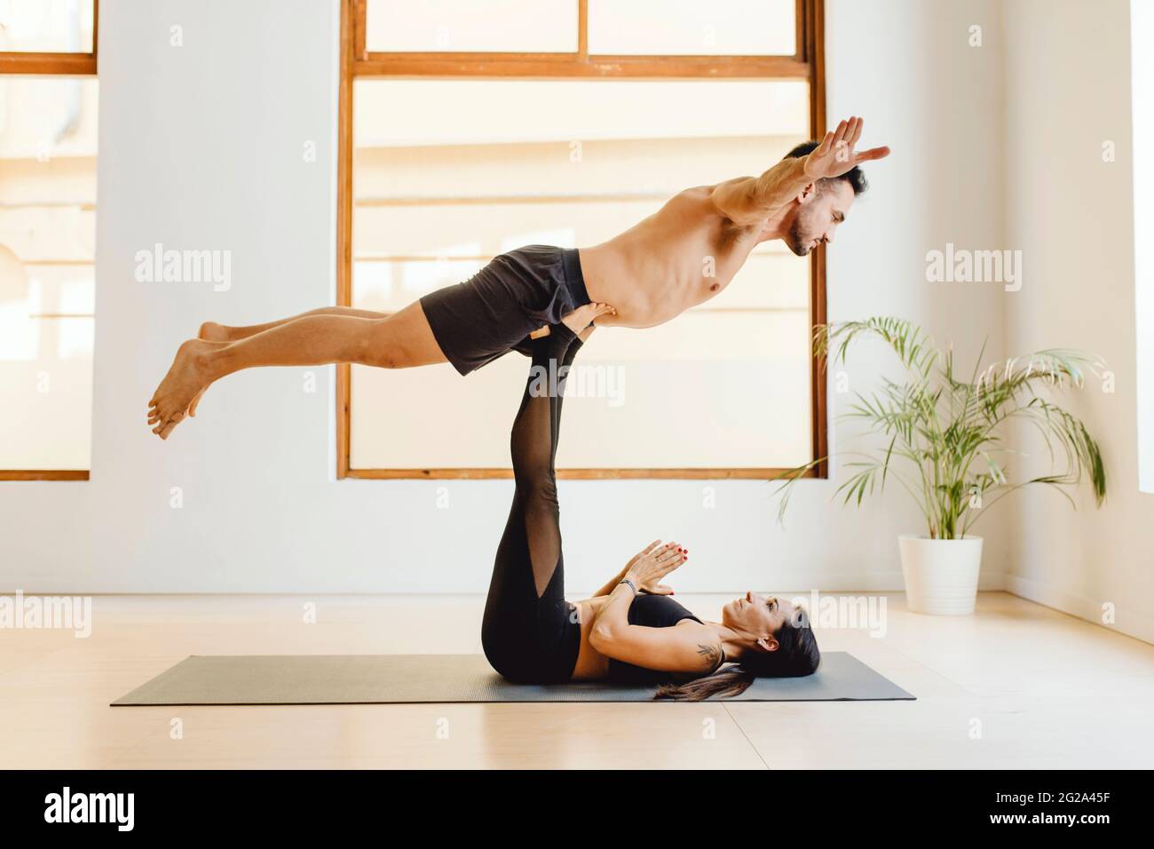 Lying on yoga mat young Woman holding muscular man on lifting legs on  lesson in training room Stock Photo - Alamy