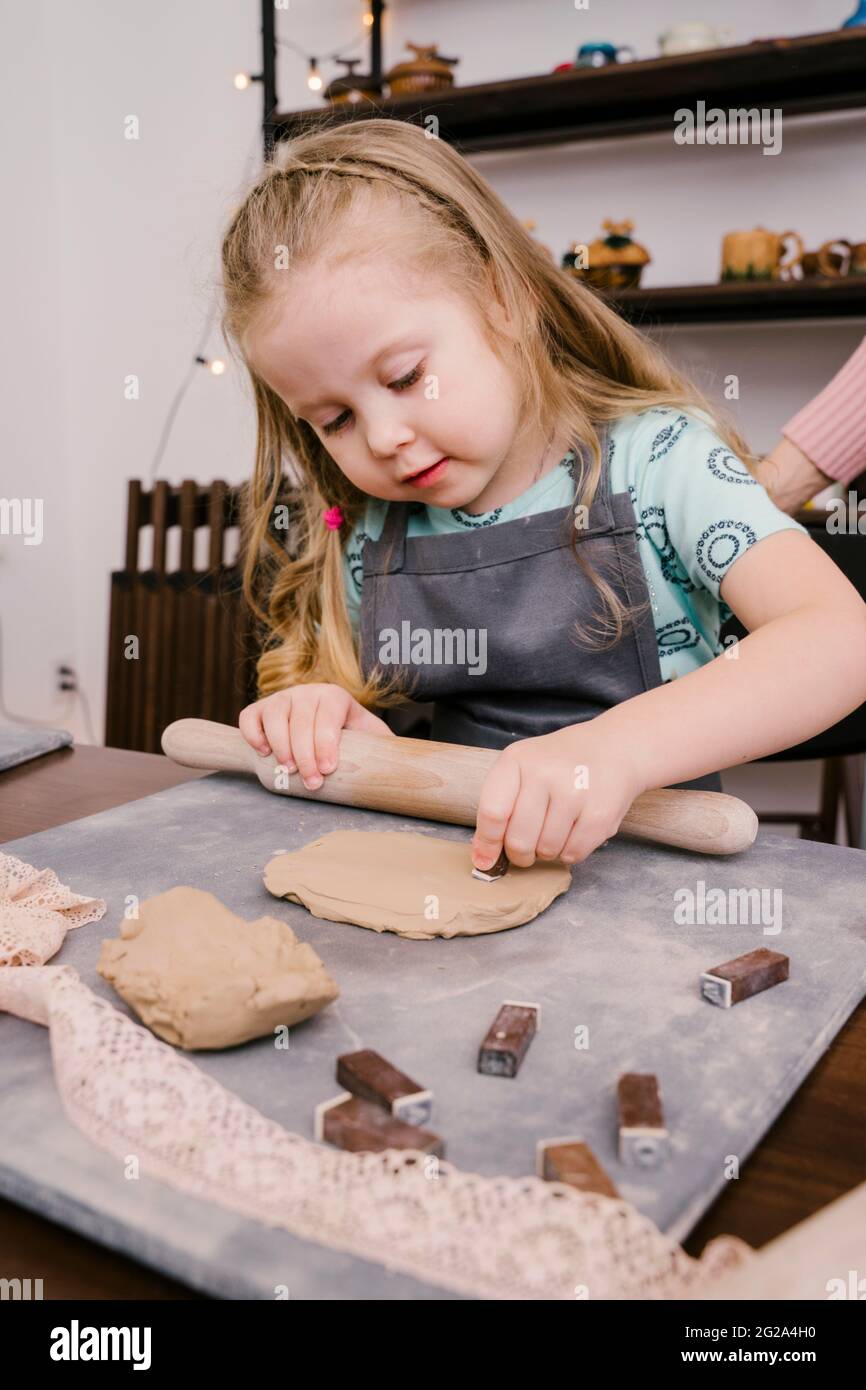 Little girl rolling clay with rolling pin in light workshop Stock Photo