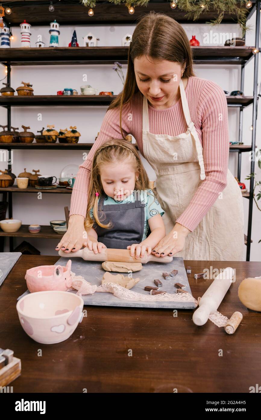 Woman craft master and girl rolling clay with rolling pin in light workshop Stock Photo