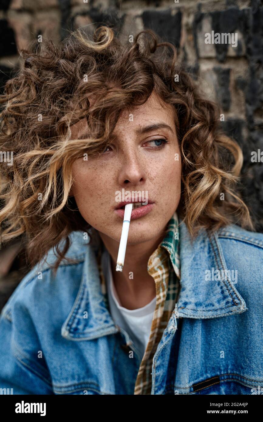 Stylish curly Woman sitting and thoughtfully smoking in abandoned place looking away Stock Photo