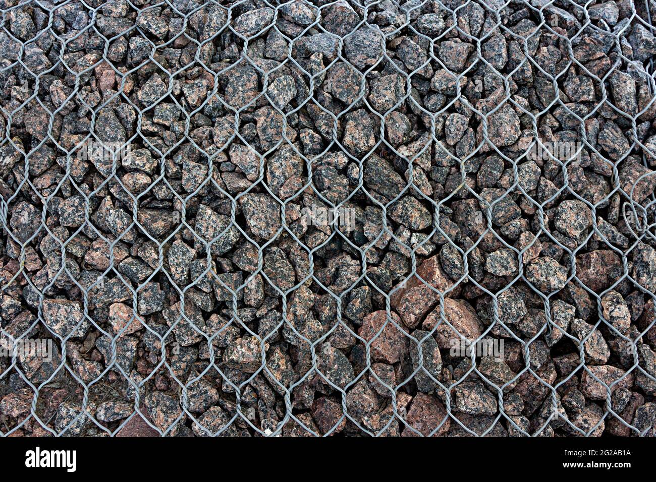 Part view of gabion fence filled with granite stones supported by chain