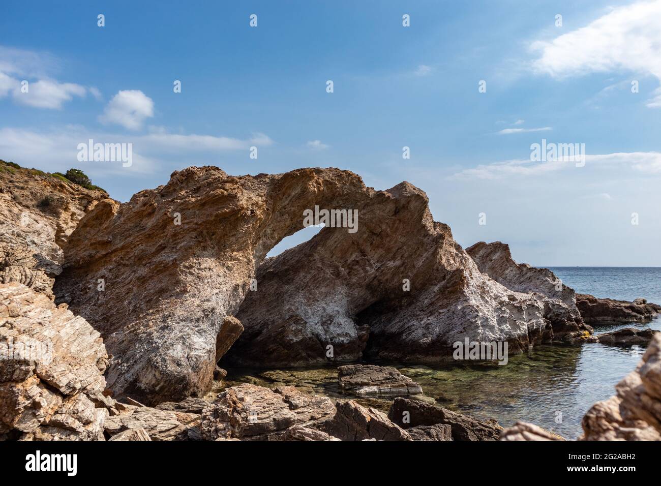 Big rock with a hole on wild mediterranean sea shore with crystal clear water. Travel Greece near Athens. Summer nature scenic lagoon Stock Photo