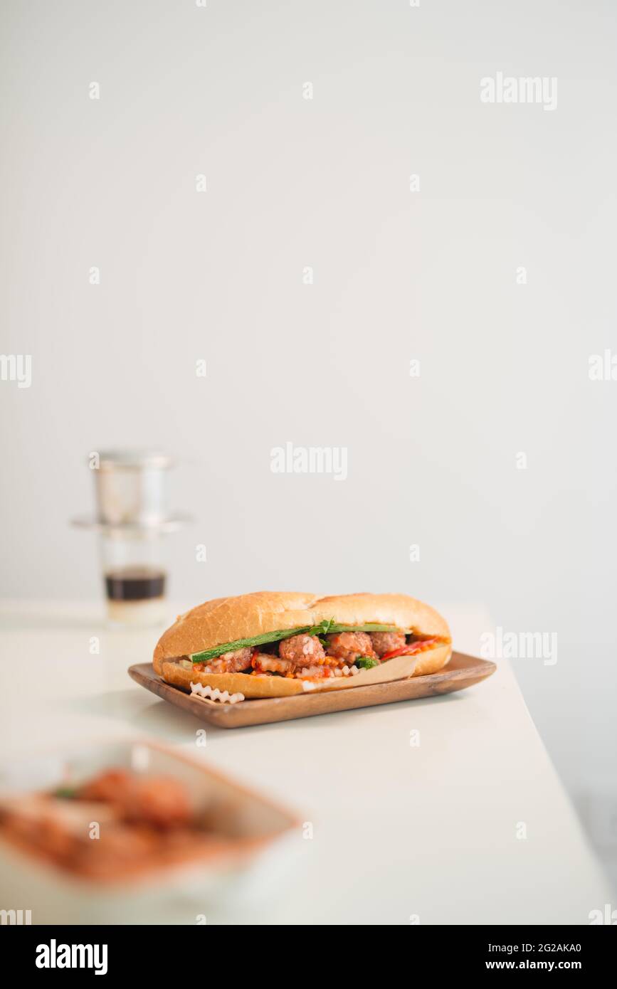 Banh Mi Xiu Mai - Vietnamese sandwich with meatballs in tomato sauce, do chua (radish and carrot pickle), cucumber and coriander. Stock Photo