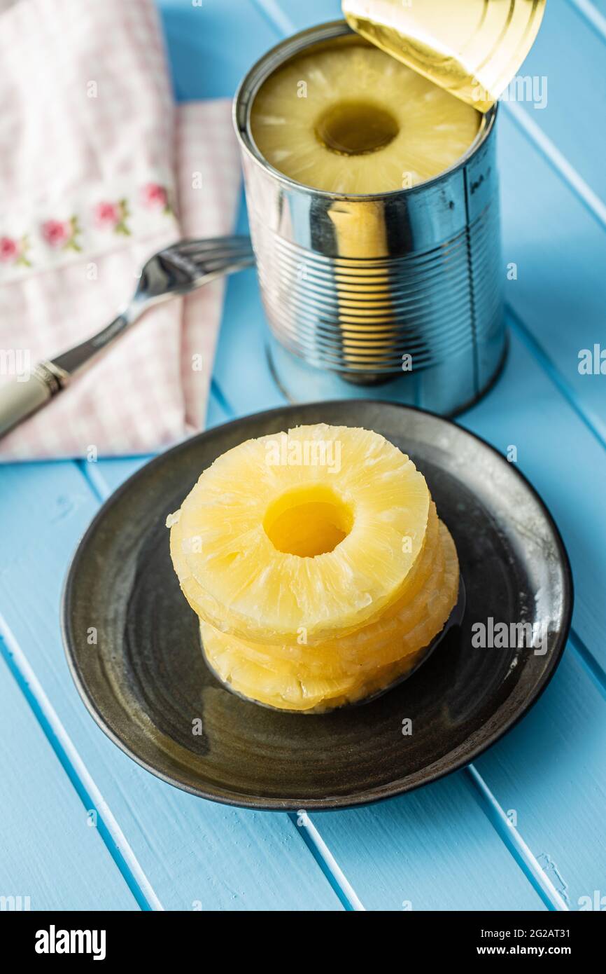 Canned sliced pineapple fruit on plate on blue table. Stock Photo