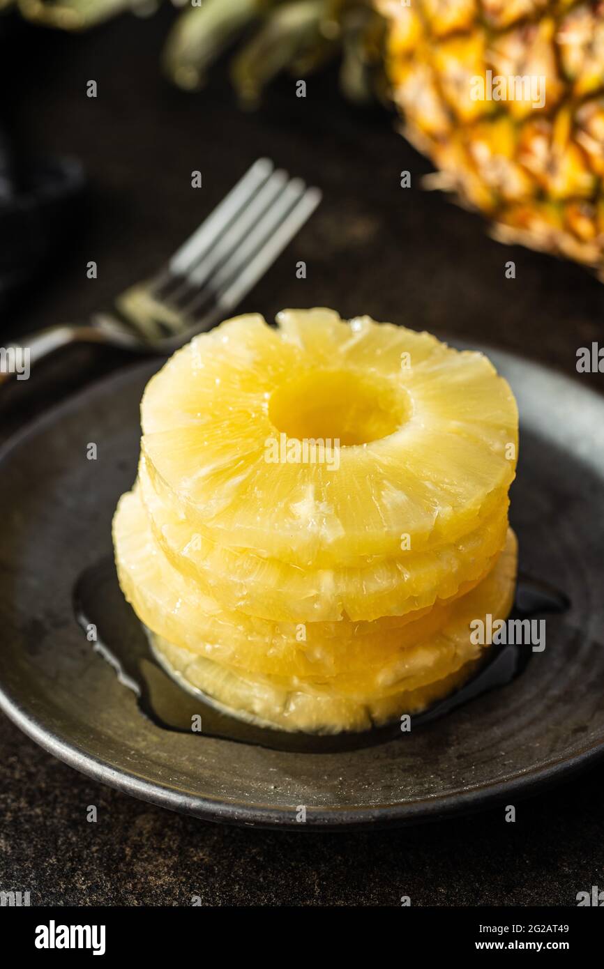 Canned sliced pineapple fruit on plate on black table. Stock Photo