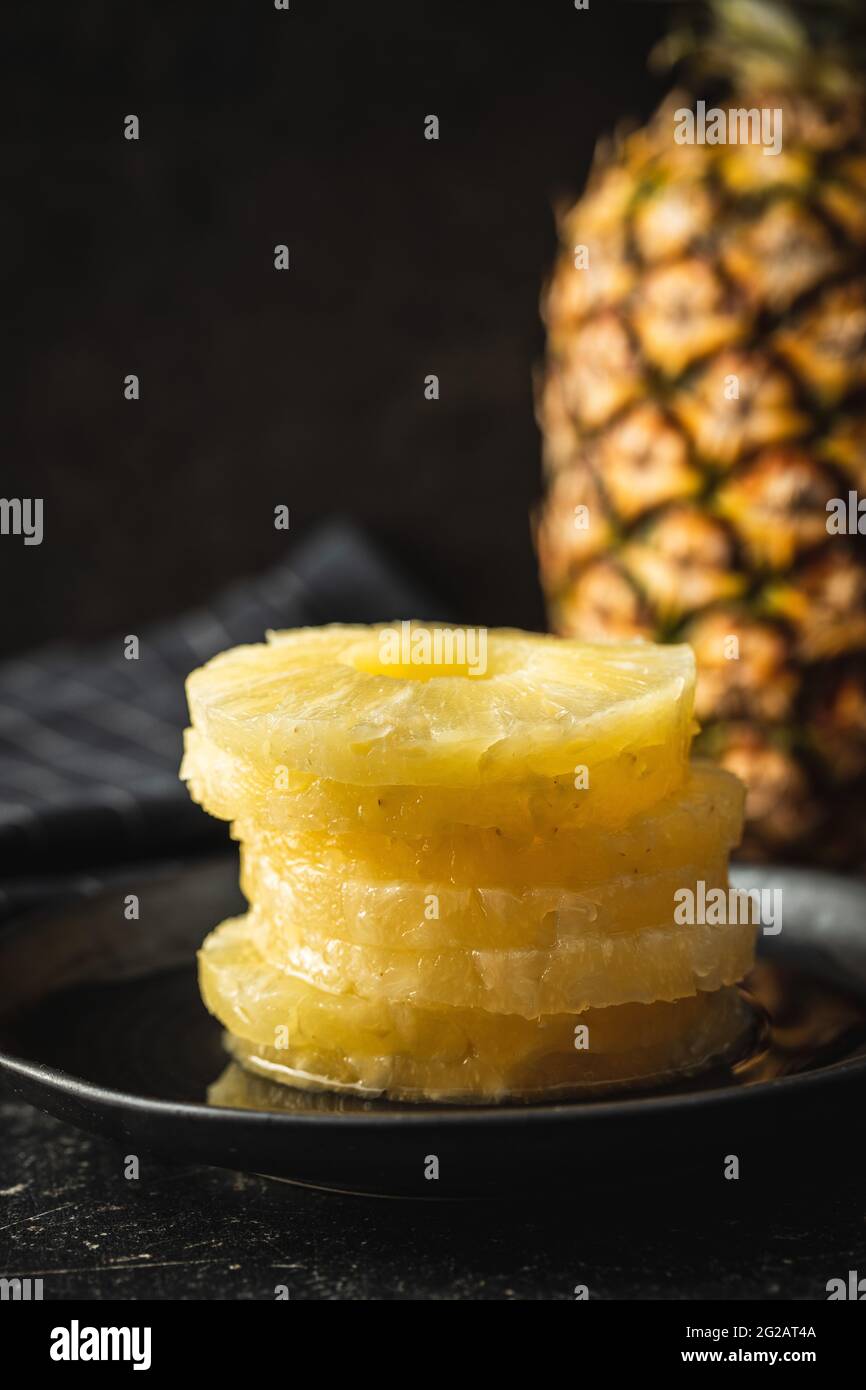 Canned sliced pineapple fruit on plate on black table. Stock Photo