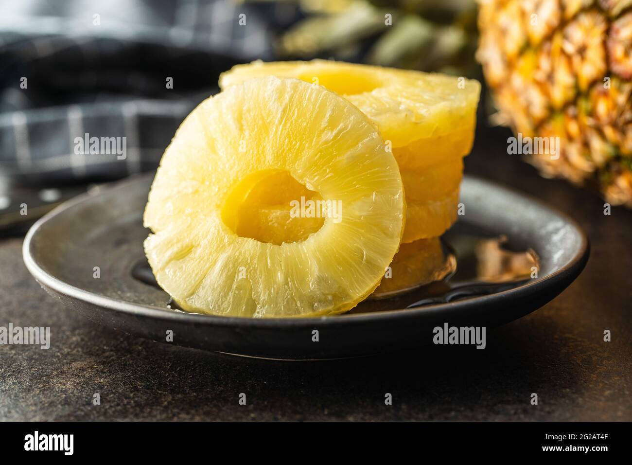 Canned sliced pineapple fruit on plate on black table. Stock Photo