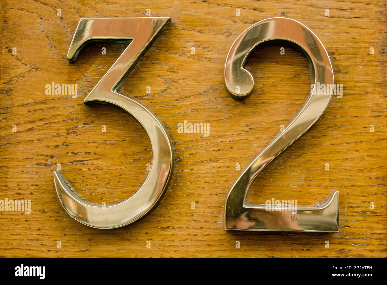 Brass number thirty two on a varnished wooden plaque on the outside wall of a building in central London. Stock Photo