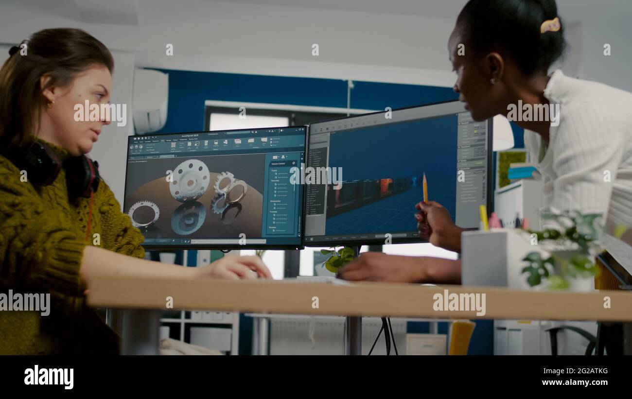 Diverse women game software developers creating game interface sitting in startup creative agency company using pc with two displays. Workers developing online video games with modern technology Stock Photo