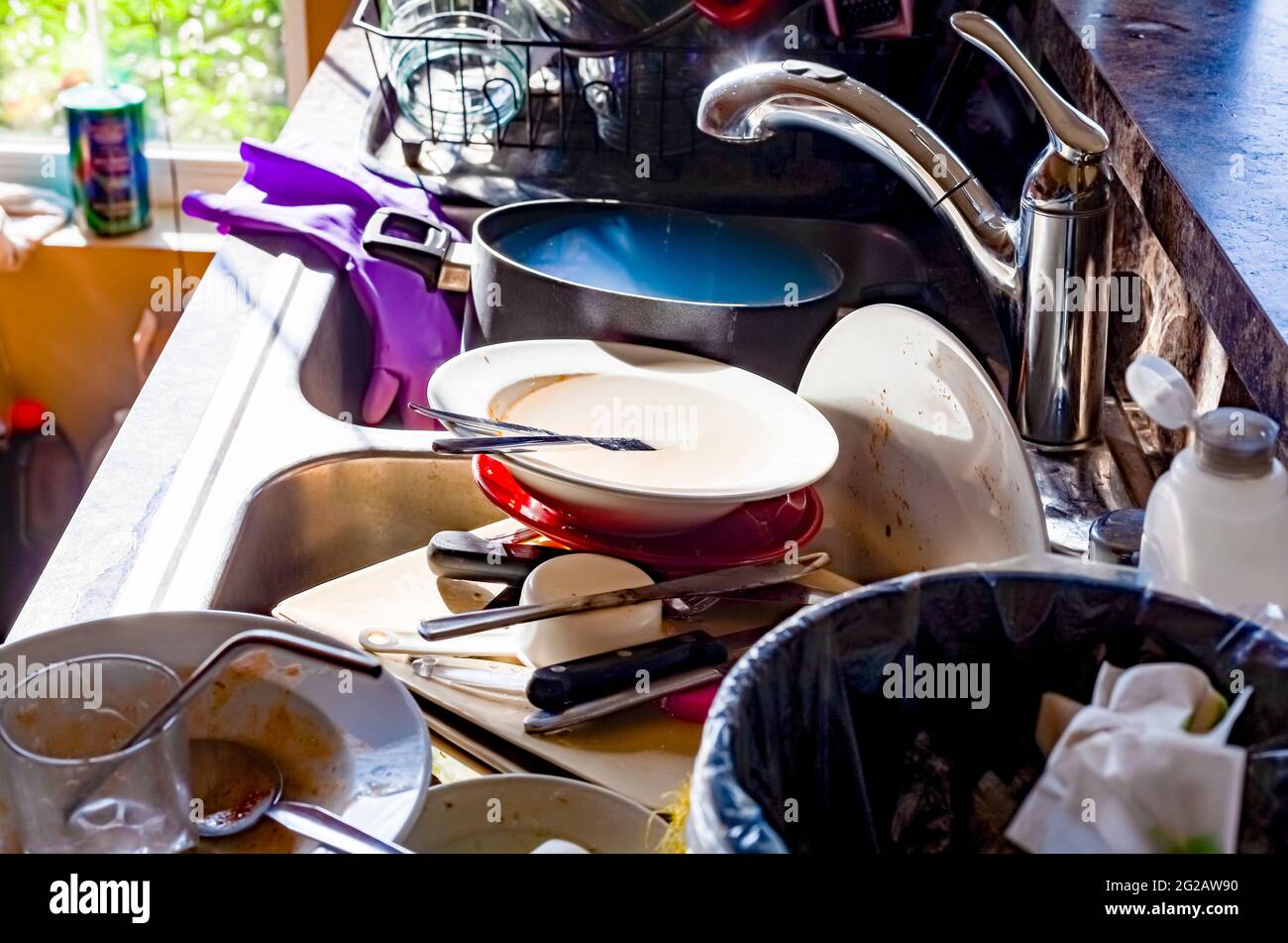 A big pile of dirty dishes, pots, utensils stacked into kitchen sink. Concept image for hand washing dishes, mess in kitchen, chores, eyesore. Common Stock Photo