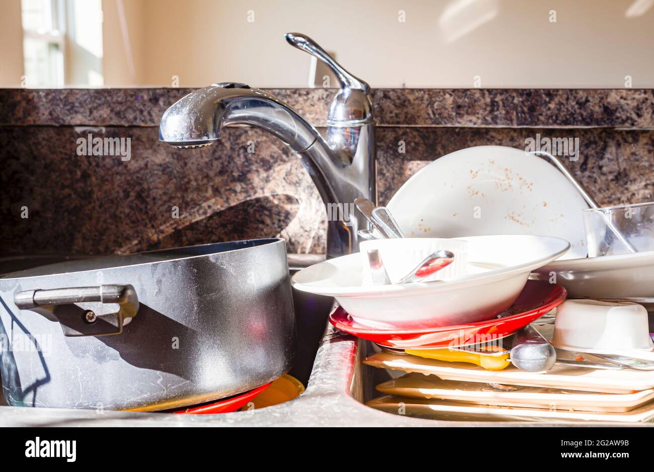 Close up frontal view of a kitchen mess with dirty pots, dishes and utensils have piled up in kitchen sink in front of the faucet. They are waiting to Stock Photo