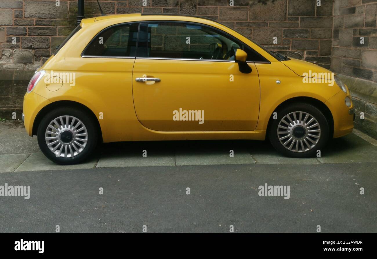 9 June 2021 - England, UK: Dark yellow Fiat 500 parked in from of old wall Stock Photo