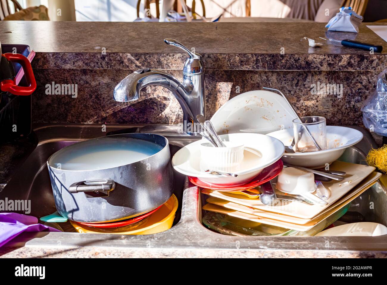 Close up frontal view of a kitchen mess with dirty pots, dishes and utensils have piled up in kitchen sink in front of the faucet. They are waiting to Stock Photo