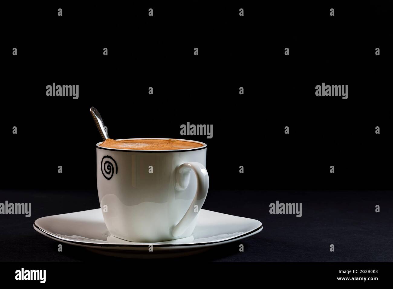 Coffee with milk in a decorative porcelain cup and with a spoon It is a horizontal photo taken on a black background with artificial light in a studio Stock Photo