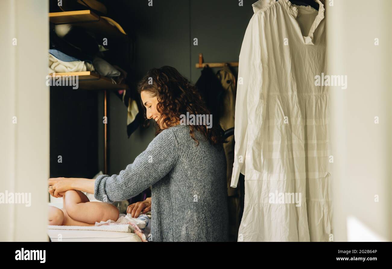 Woman changing diaper of her baby. Smiling mother changing baby diaper at home. Stock Photo