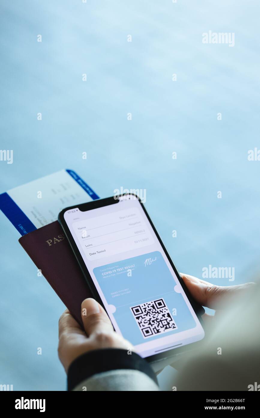 Closeup of a woman passenger with digital medical pass on her mobile with passport and plane ticket. Female traveler using digital covid rapid test re Stock Photo