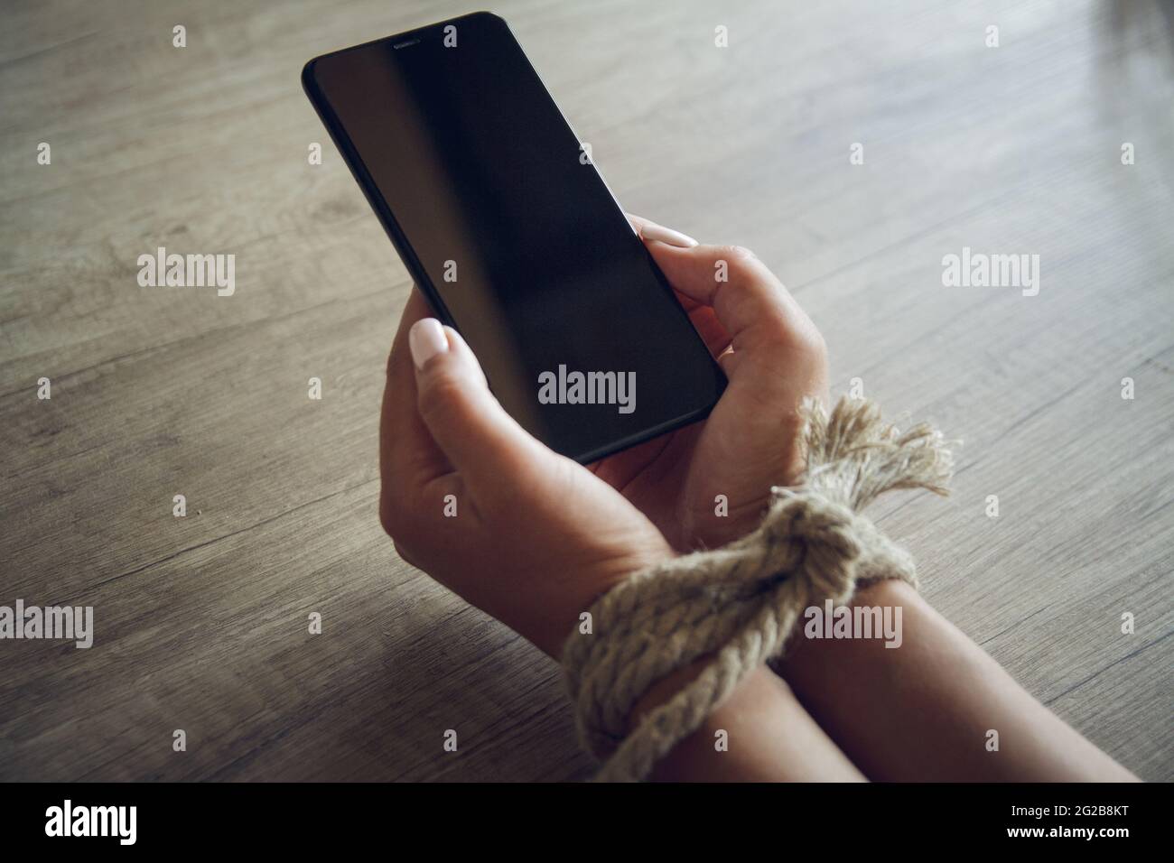 Tied female hands are holding a mobile phone. Mobile phone addic Stock Photo