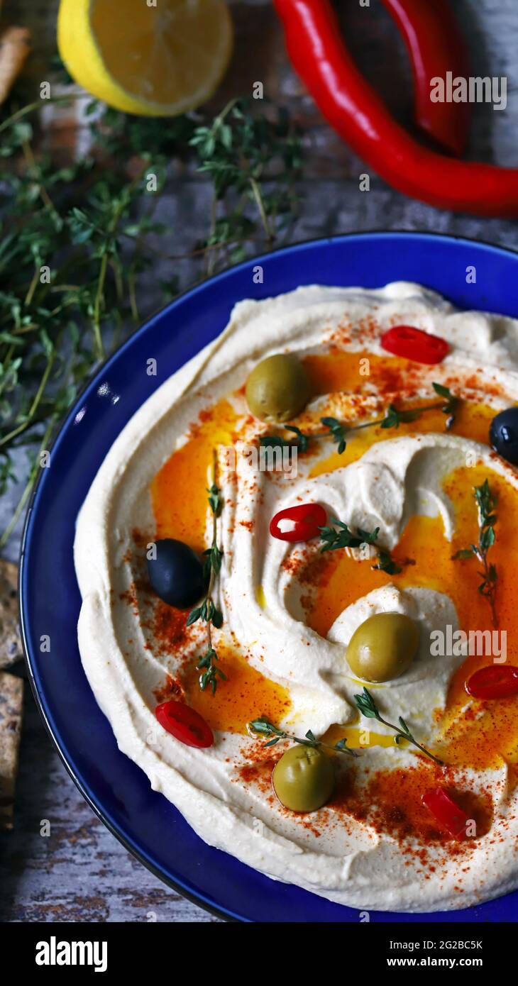 Hummus with olives, paprika and olive oil in a blue plate. A