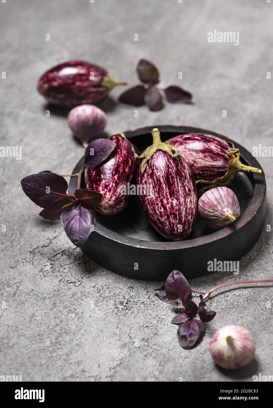 Organic raw purple mini eggplants with garlic and basil on grey stone background Stock Photo