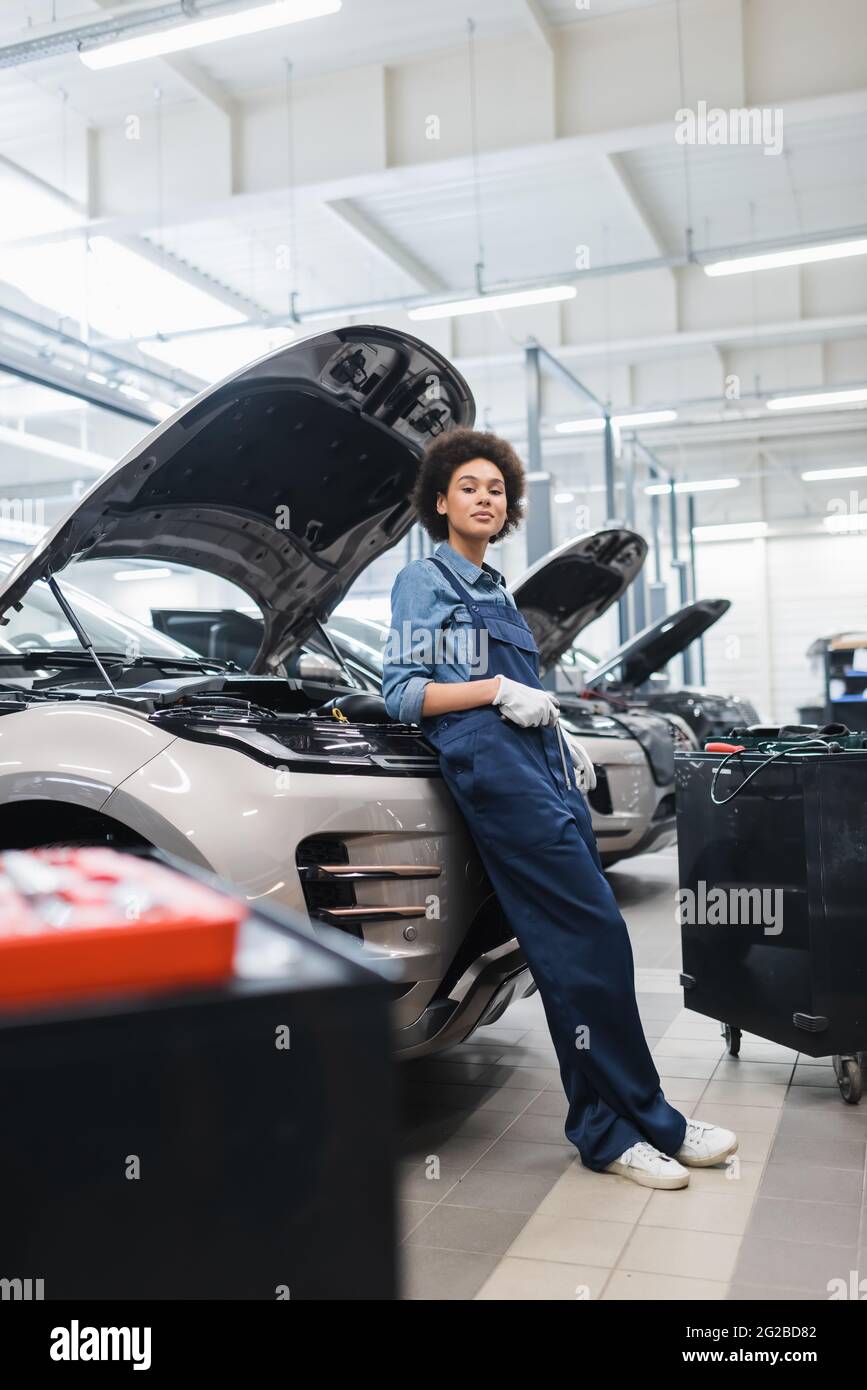 young african american mechanic standing near cars with open hoods in auto repair service Stock